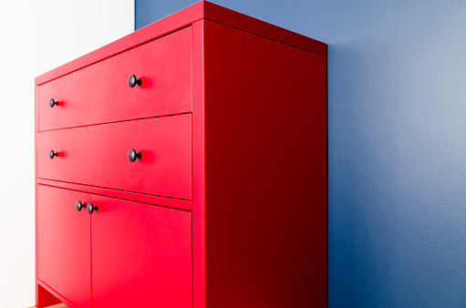 Red wooden chest of drawers in Scandinavian style against a blue wall. Interior design