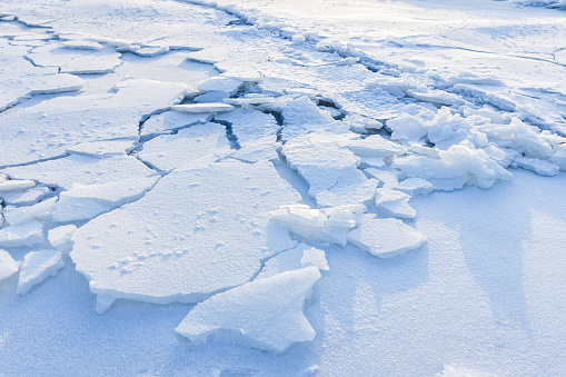 Cracked ice hummocks covered with snow. Broken ice fragments lay on the coast of frozen Baltic Sea on a winter day