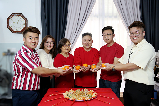 Asian family members holding tangerine fruit prior to 'YuSheng' (Yee Sang or Prosperity Toss) at home. Tangerine fruit signifies Gold in Chinese culture.