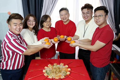 Asian family members holding tangerine fruit prior to 'YuSheng' (Yee Sang or Prosperity Toss) at home. Tangerine fruit signifies Gold in Chinese culture.