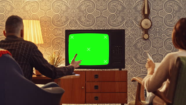 DS Man watching an old tv set with green screen and woman reading