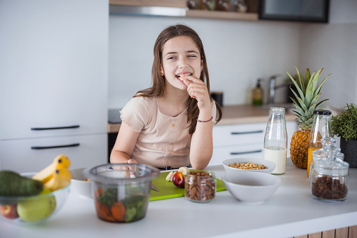 Teenage girl standing in the kitchen and eating fruit