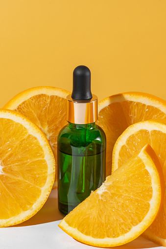 Natural vitamin c serum, skincare, essential oil products. Cosmetic green glass dropper and fresh juicy orange fruit slice on orange background. Beauty product branding mock-up