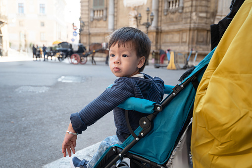 Curious toddler explores the streets of Palermo, Italy, his tiny face filled with wonder as he sits in his stroller, surrounded by the vibrant colors and bustling energy of the city. Baby boy traveler sitting in a stroller and observing the architecture of Palermo