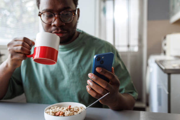 African American man drinking coffee, eating oatmeal and using smart phone