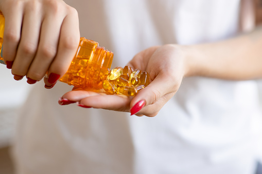 Woman pouring fish oil capsules from bottle