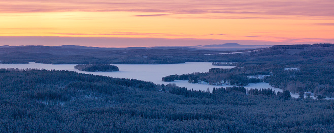 A forest and lake landscape on a winter morning in the Dalarna region of Sweden.