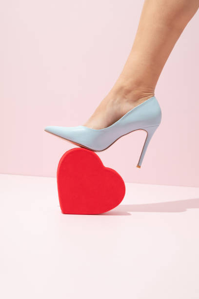 red patent leather shiny women's stiletto heels on black wooden table and red and black background with glowing hearts and bokeh