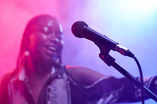 Close up of microphone on stage with Black young woman singing in blurred background copy space