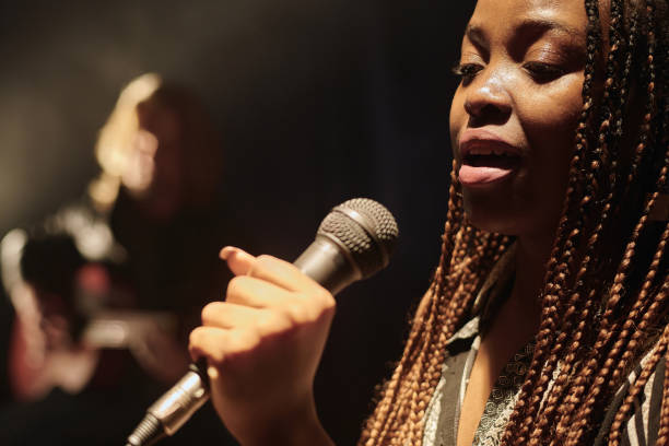 Side view portrait of young African American singer holding microphone and performing on stage in spotlight copy space