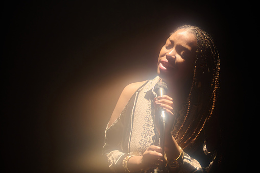 Waist up portrait of talented Black woman singing on stage in glowing spotlight copy space