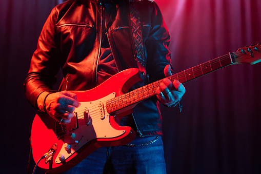 Cropped shot of unrecognizable rock musician playing electric guitar on stage and wearing leather jacket copy space