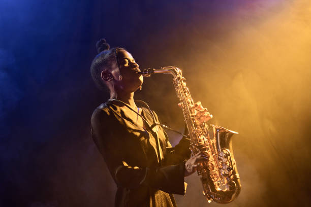 Black Woman Performing in Jazz Nightclub Portrait of passionate Black woman musician playing saxophone in jazz nightclub with golden hazy light copy space sax arts and crafts stock pictures, royalty-free photos & images