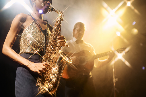 Close up of jazz music duo band performing on stage during live music concert with young woman playing saxophone in foreground, copy space