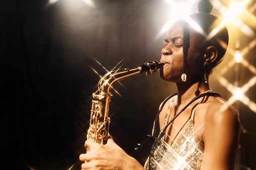 Side view portrait of young woman playing saxophone music on stage in golden lights copy space