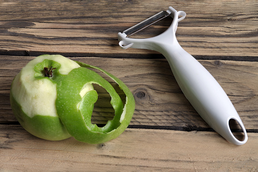 Knife for cleaning fruits and vegetables with apple with peeled skin on a background of rough wooden texture.