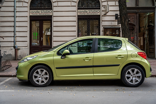 Side view of an ordinary Peugeot 207 5-door hatchback (pre-facelift) in beautyful green metallic color. 30.09.2023, Subotica, Serbia