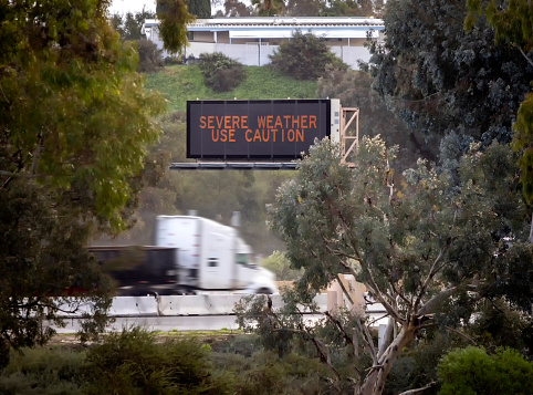 Digital road sign stating Severe Weather Use Caution with a truck passing under it. The shot is on the 15 freeway in Escondido California
