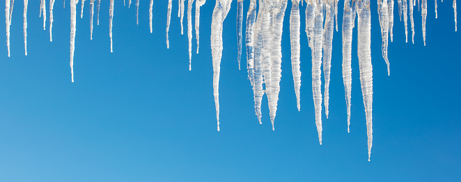 Close-up of shiny icicles on a blue sky background. Space for copy.