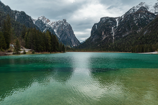 Moody landscape with turquoise water alpine lake Lago di Dobbiaco in Dolomites mountains, Cortina dAmpezzo, Italy on cloudy spring day. Lake Toblacher See in the forest in Dolomiti in Italian Alps.