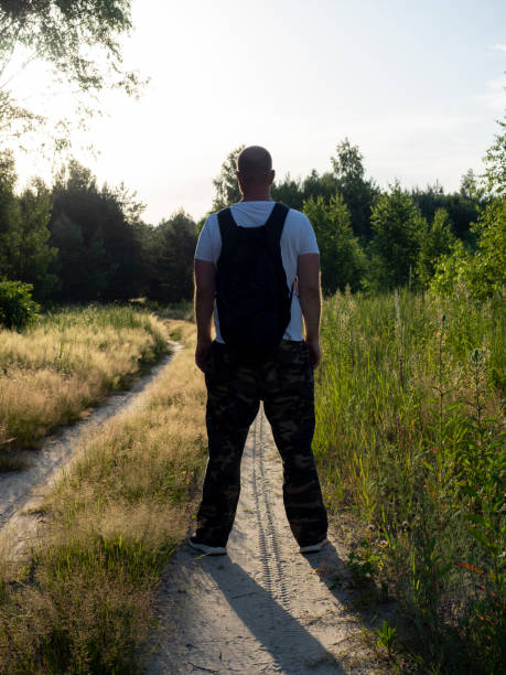 istock A man with a backpack on his back is standing on a forest path with his back to the camera. Evening, the silhouette of a man in the shade 2008366943