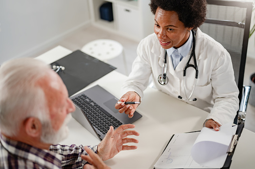 Doctor specialist consulting a patient in a doctor's office at a clinic. Female doctor is talking with a male elderly patient.