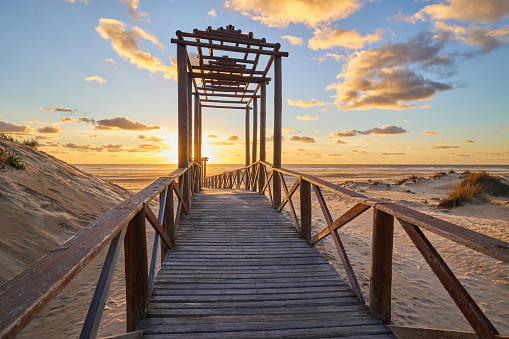 Dramatic sea sunset. The blinding sun hid behind the arch of the wooden bridge. The setting sun sinks into the sea