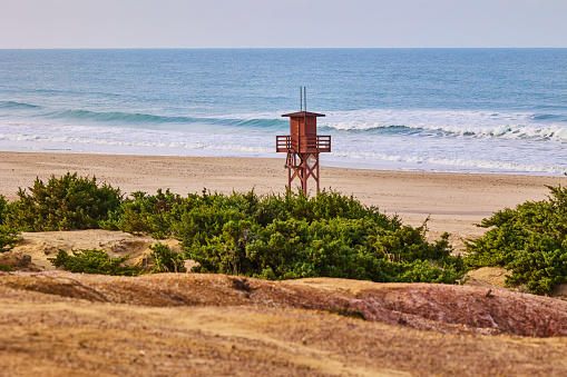 Dark red wooden lifeguard tower and empty sandy beach on the seashore in the off season.