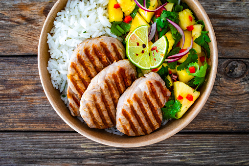 Grilled pork loin steaks with rice and mango salad in lunch box to go on wooden background