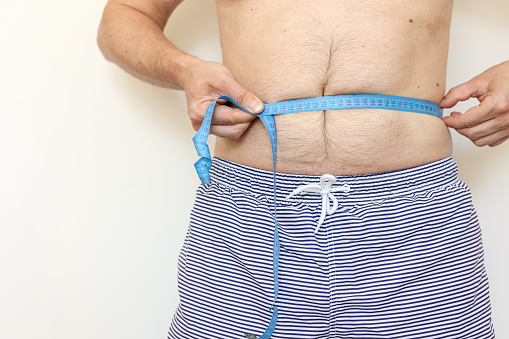 Man measures his fat belly with measuring tape and shows thumb up. Concept of weight loss, health problems of obese people. Controlling eating and active lifestyle. World Obesity Day.