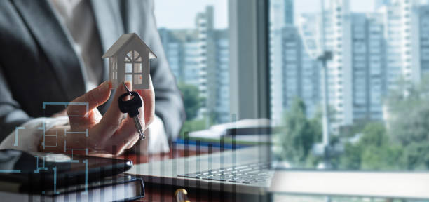 real estate agent shows a house and the keys to it. real estate agent shows a house and the keys to it on a blurred office background. turnkey project stock pictures, royalty-free photos & images