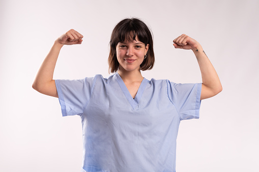 Studio portrait with white background of a young female proud doctor showing bicep to prove strength