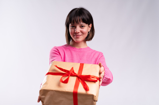 Studio portrait with white background of a woman giving a present looking to the camera