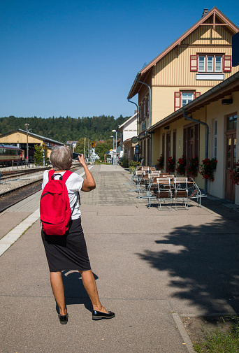 A beautiful elderly woman visiting city in Germany. She photographs the picturesque railroad station building. Live in the present