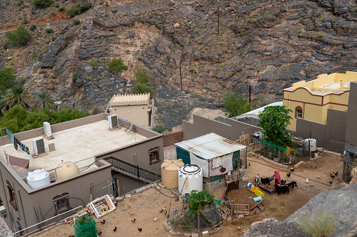 Bilad Sayt, Oman - 25 October 2023: View from above on rooftops. Local women tending her domestic animals. Old village Bilad Sayt in Al Hajar Mountains. Oman