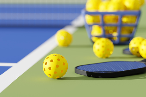 Pickleball sport equipments, paddle and basket of balls on court. 3d illustration, render. Selective focus