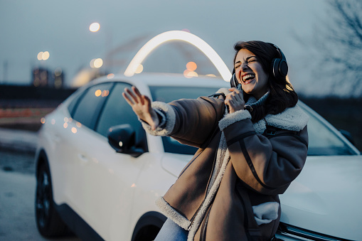 Woman dancing, singing and listening music while leaning on car