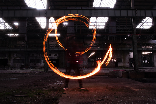 Fire dancer performing fire dance in long exposure in an old and abandoned industrial building.