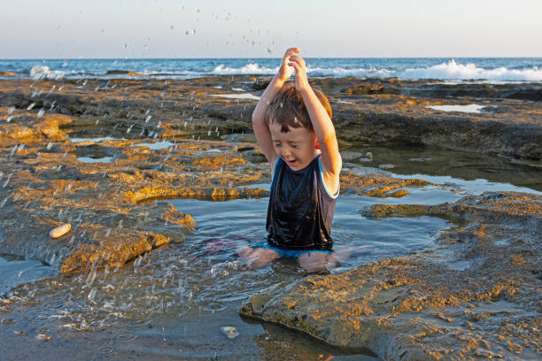 A child playing with water on the beach, on the rocks.