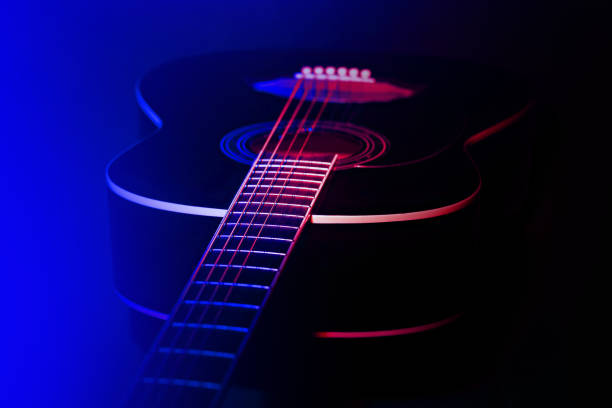 Man plays his guitar on a theater stage with colored lights, smoke around, playing beautiful notes for the audience, in a provided concert and sometimes he performs songs with his beautiful voice