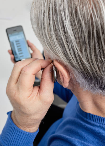 istock Elderly man with hearing loss with behind-the-ear hearing aid adjusting device settings using mobile application. Innovations in hearing aid technology 2008546048
