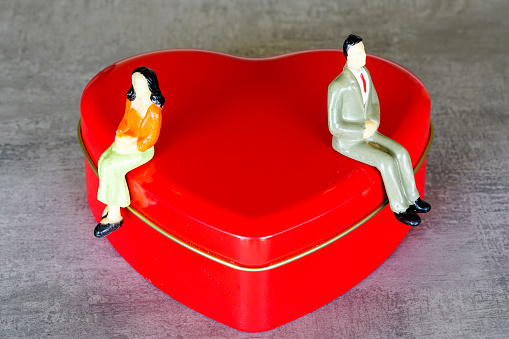 Quarrelled miniature female and male figures sit on different sides of a large red heart shape figure, quarrel concept