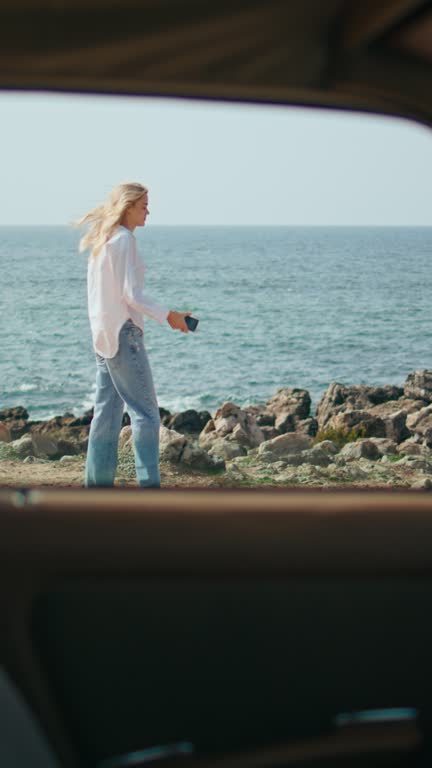 Unknown woman walking coast with phone view through car window vertical oriented