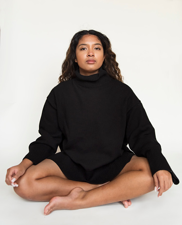 Portrait of beautiful asian teenager on white background. She is 16 year’s old, and has long curly brown hair. She is wearing a black wool turtleneck and black shorts, sitting on the floor. Vertical full length studio shot with copy space. This was taken in Montreal,  Quebec, Canada.