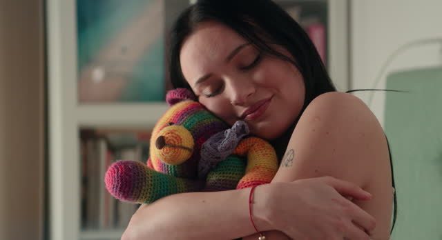 Woman in bed embracing a rainbow LGBT teddy bear stuffed animal plush