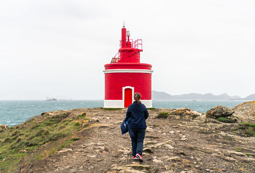Woman hiking on the cliffs near a red lighthouse