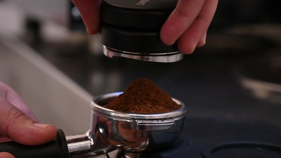 Barista hand holding and pressing tamper on coffee grounds powder in portafilter ready to make cup of coffee