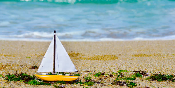 istock Toy sail boat on sand shore with sparkling light blue sea background. 2008681224