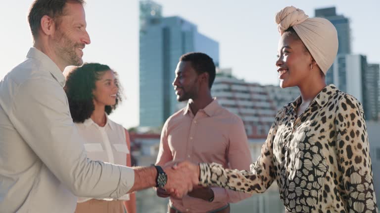 Business people, rooftop and handshake in city with team for partnership, meeting or outdoor greeting. Happy businessman and woman shaking hands for b2b, agreement or deal together in an urban town