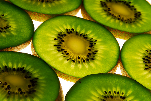kiwi slice against light, close up view, green color fruit on white background